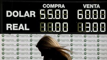 Una mujer camina frente a un tablero que muestra la tasa de cambio en Buenos Aires, Argentina.