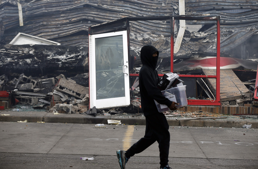 Un hombre carga unos objetos mientras camina frente a una tienda de Auto Zone quemada, el jueves 28 de mayo de 2020, en Minneapolis, Minnesota.&nbsp;