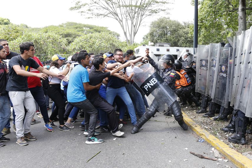 Un polic&iacute;a nacional trata de eludir a un grupo de estudiantes en las afueras de la Universidad Central de Venezuela en Caracas, el jueves 14 de noviembre de 2019.&nbsp;