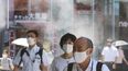 Gente con mascarillas para protegerse contra la expansión del coronavirus caminan bajo agua vaporizada en Tokio, el jueves 5 de agosto de 2021.&nbsp;