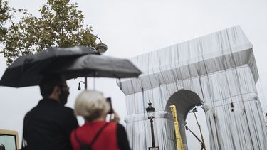 Dos personas miran cómo varios trabajadores envuelven en tela el monumento del Arco de Triunfo, en París, el miércoles 15 de septiembre de 2021.