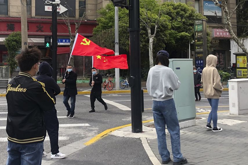En esta imagen de archivo, residentes pasean con la bandera del Partido Comunista mientras otros hacen fila para someterse a una prueba de detección del coronavirus, en el distrito de Jingan, en Shanghái, China, el 1 de abril de 2022.&nbsp;