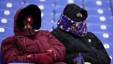 Dos personas de cobijan del frío en el partido de fútbol americano entre los Ravens de Baltimore y los Texans de Houston, en Baltimore, el 20 de enero de 2024. 