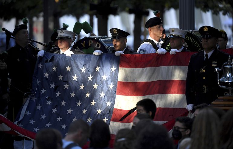 Policías y bomberos de Nueva York sostienen una bandera estadounidense mientras una banda toca el himno nacional en el monumento nacional conmemorativo del 11 de septiembre, durante la ceremonia del 20º aniversario de los atentados del 11-S en el World Trade Center, en Nueva York, el 11 de septiembre de 2021. 