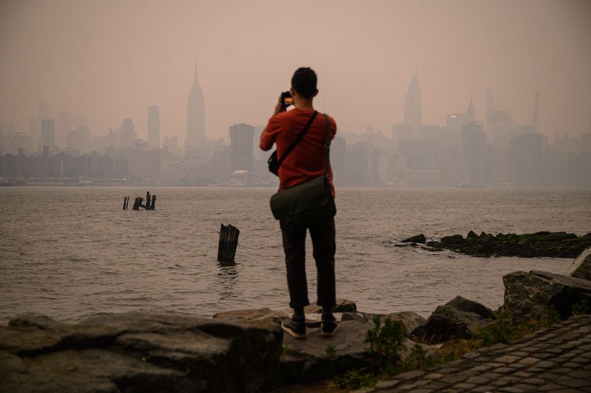 Un hombre frente al horizonte de la ciudad de Nueva York y el East River envueltos en humo, en Brooklyn el 6 de junio de 2023, a causa de los incendios en Canadá.   