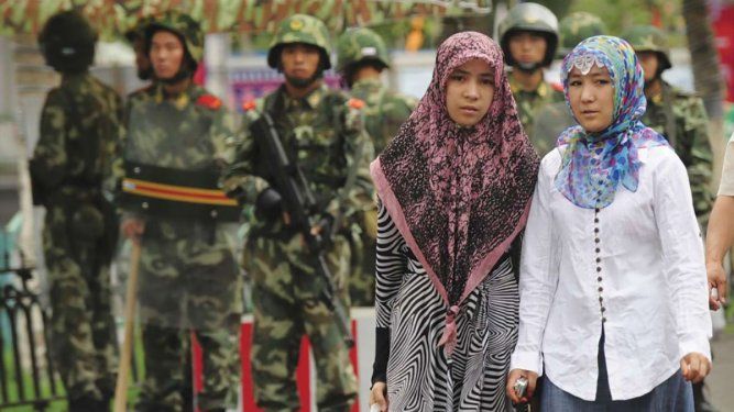 Mujeres de la etnia uigur vigiladas por militares chinos.