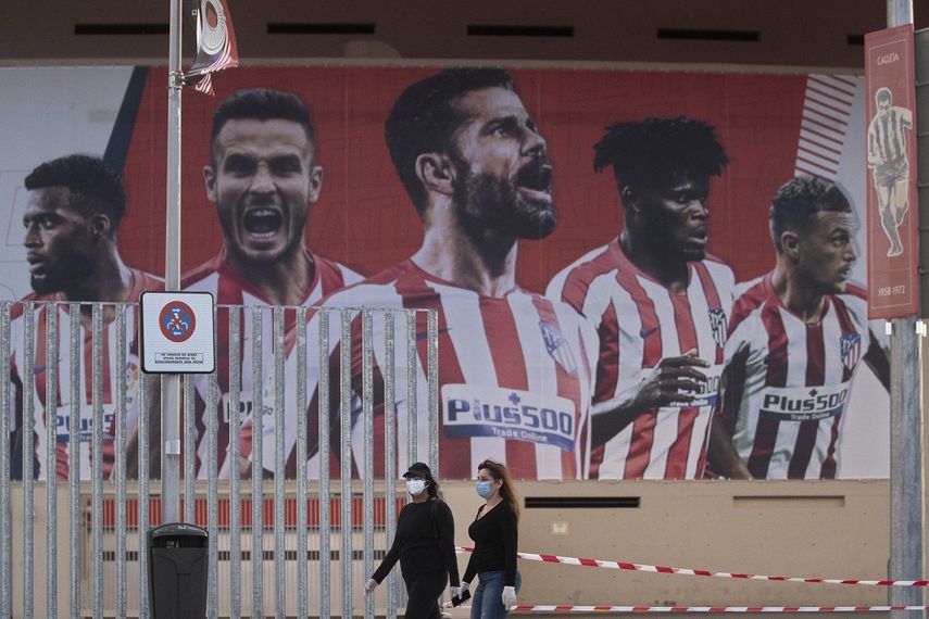 En esta foto del 5 de mayo de 2020, dos mujeres con mascarillas pasan frente a un afiche gigante con la imagen de jugadores del Atl&eacute;tico de Madrid en el estadio Wanda Metropolitano.&nbsp;
