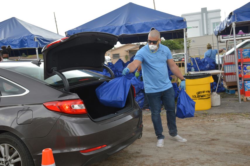 Voluntario coloca alimentos en maletero de autom&oacute;vil.