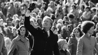 El presidente estadounidense Jimmy Carter saluda a la multitud mientras camina con su esposa Rosalynn, y su hija, Amy, a lo largo de la Avenida Pennsylvania tras su investidura, el 20 de enero de 1977, en Washington.&nbsp;