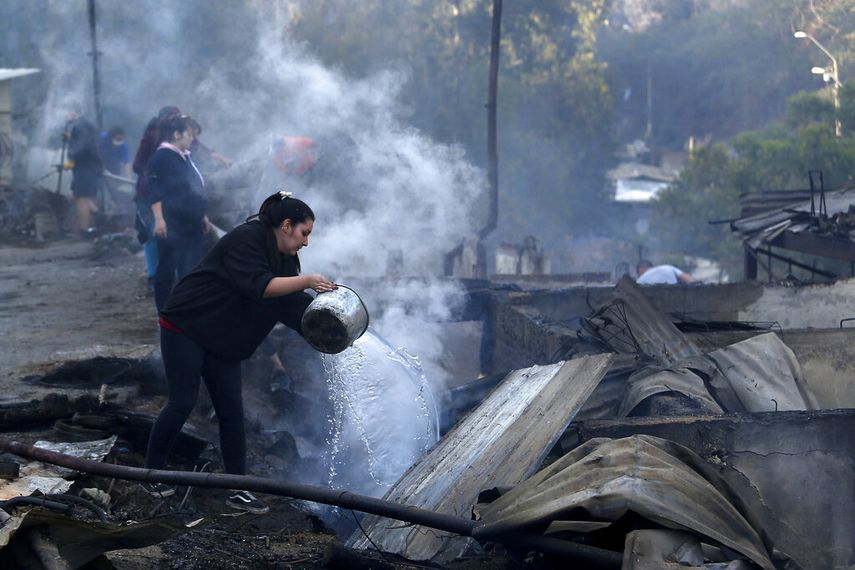 Residentes arrojan agua sobre los restos de sus casas despu&eacute;s que un incendio da&ntilde;&oacute; decenas de viviendas en las afueras de Valpara&iacute;so.