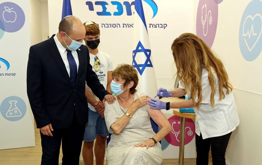 El primer ministro israelí Naftali Bennett acompaña a su madre Mirna Bennett a ponerse la tercera vacuna contra el coronavirus en Haifa, Israel.