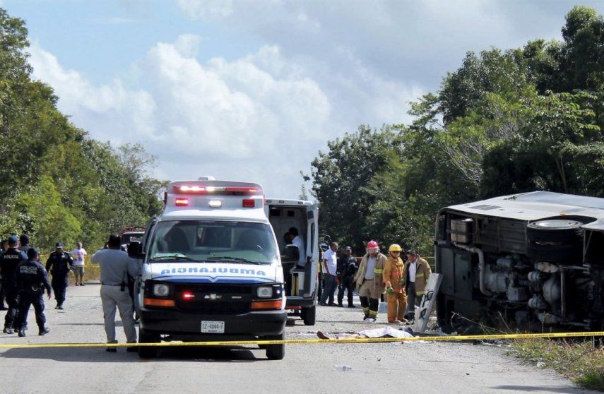 El cuerpo sin vida de un pasajero yace al lado de un autobús que volcó.