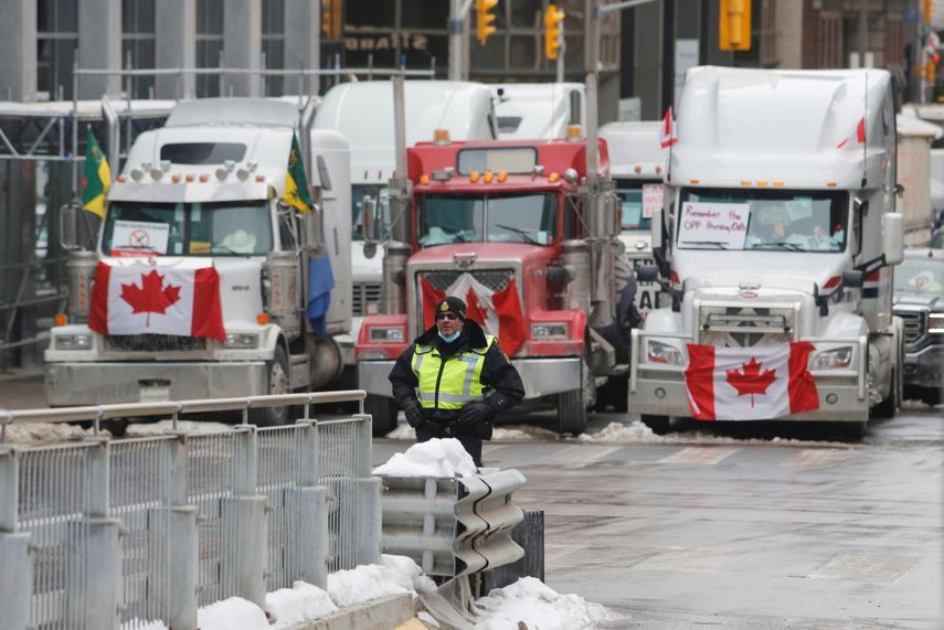 Un policía de pie frente a camiones que bloquean el paso hacia las calles del centro como parte de una protesta contra las medidas impuestas por el COVID-19, el miércoles 9 de febrero de 2022, en Ottawa.&nbsp;