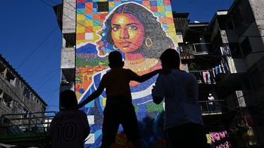 Niños miran un mural hecho con tapas de botellas de plástico por el artista venezolano Oscar Olivares en un edificio de apartamentos en el barrio Zacamil en Mejicanos, El Salvador, el 20 de febrero de 2026.