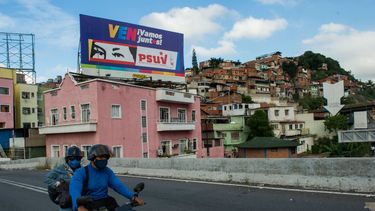 La gente pasa en bicicleta frente a una valla publicitaria con propaganda política que representa los ojos del fallecido presidente venezolano Hugo Chávez, en Caracas el 2 de diciembre de 2020 antes de las elecciones parlamentarias en el país. Venezolano celebrará elecciones legislativas el 6 de diciembre.