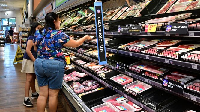 Una madre y su hija miran los precios de productos cárnicos en un supermercado.