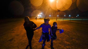 Tres migrantes se toman de las manos mientras corren bajo la lluvia en una zona de detención después de entregarse a las autoridades luego de cruzar la frontera desde México hacia Estados Unidos en Roma, Texas.