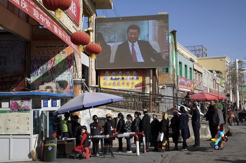 En esta imagen de archivo del 3 de noviembre de 2017, vecinos esperando en fila en un control de seguridad en el bazar Hotan, donde una pantalla muestra al presidente de China, Xi Jinping, en Hotan, en la región occidental china de Xinjiang. 