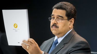 El dictador venezolano Nicolás Maduro sostiene un cuaderno con el logo de la criptomoneda petro.