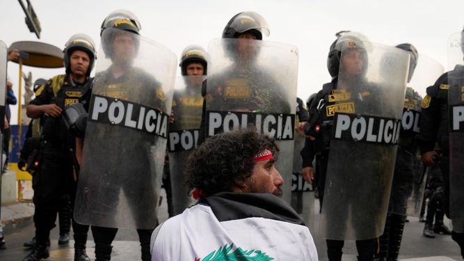 Un hombre se sienta en la calle frente a una línea de policías con equipos antidisturbios durante una marcha contra la presidenta peruana Dina Boluarte en Lima, Perú, el martes 17 de enero de 2023.