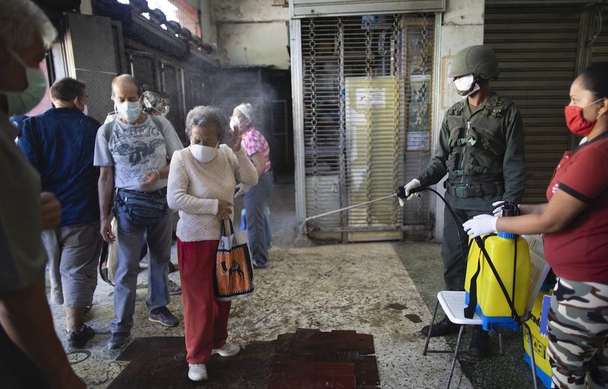 Una mujer de edad avanzada, con una m&aacute;scara facial protectora, es rociada con una soluci&oacute;n desinfectante de cloro por un soldado como medida preventiva contra la propagaci&oacute;n del nuevo coronavirus COVID-19, a la entrada de un mercado de alimentos en Caracas, Venezuela, el viernes 20 de marzo de 2020.&nbsp;