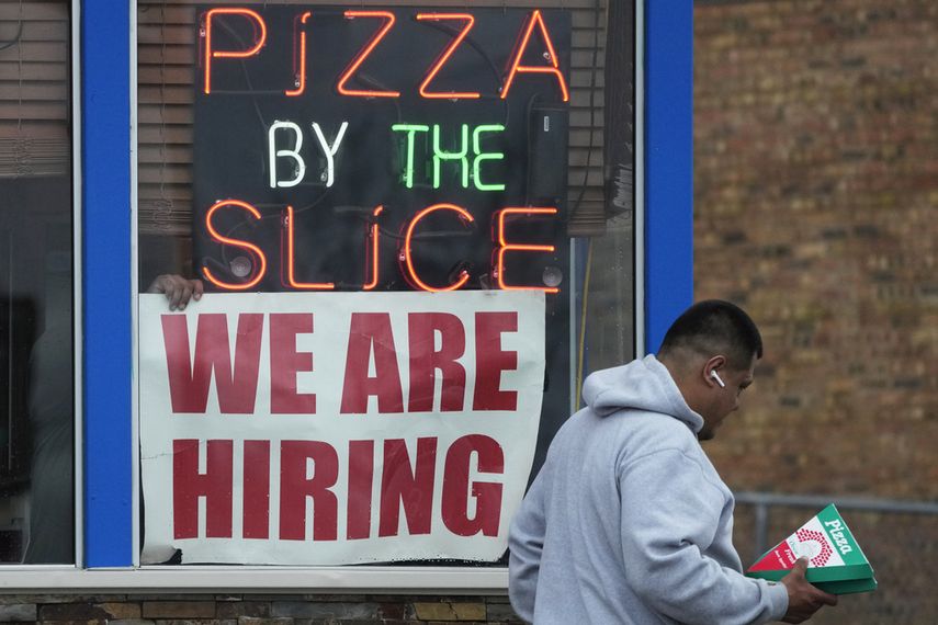 Un hombre pasa frente a un letrero que solicita empleados en una pizzería.